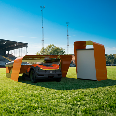 CEORA Mähroboter fährt in seine Garage auf einem Sportplatz, mit einem weiteren Gerät und Stadiontribünen im Hintergrund.