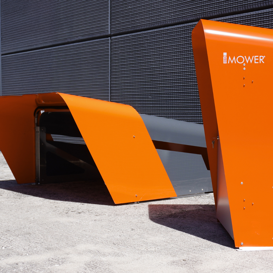 Close-up of the CEORA robotic mower garage showing the “Mower” logo on the bright orange panel.