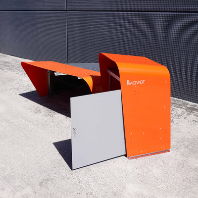 Außeninstallation des technischen Schranks für Mähroboter neben der Garagenstruktur. Das auffällige orangene Design schützt Werkzeuge und Ersatzteile mit einem Schloss an der Front.